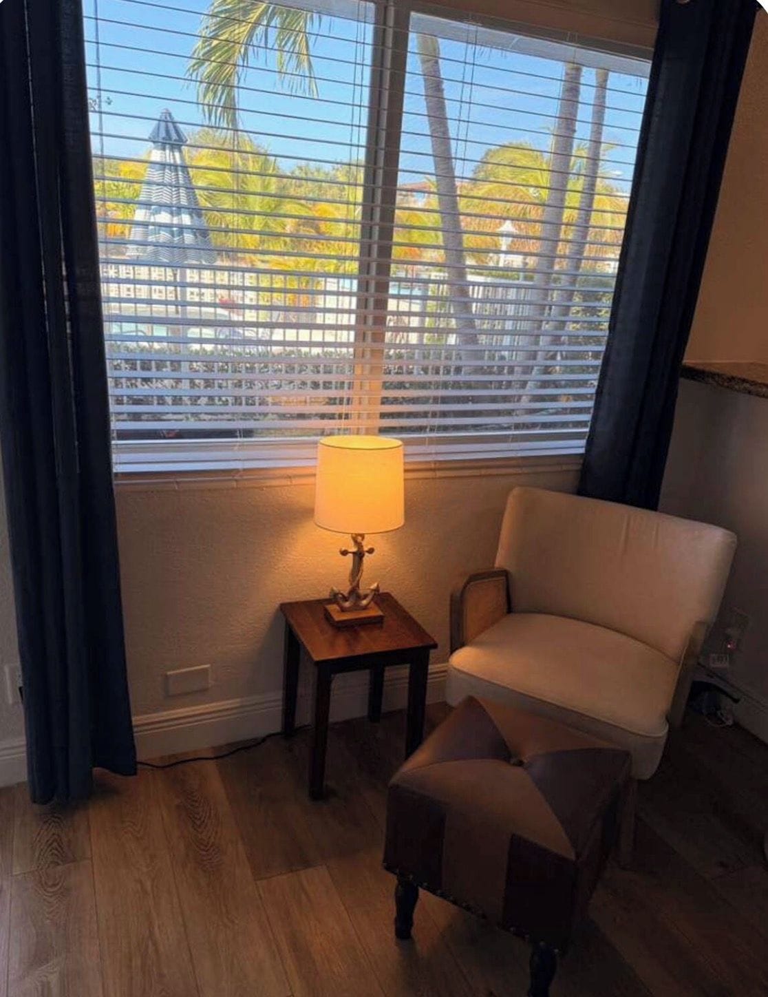 A room with a window, a lamp, a chair, and a small ottoman.