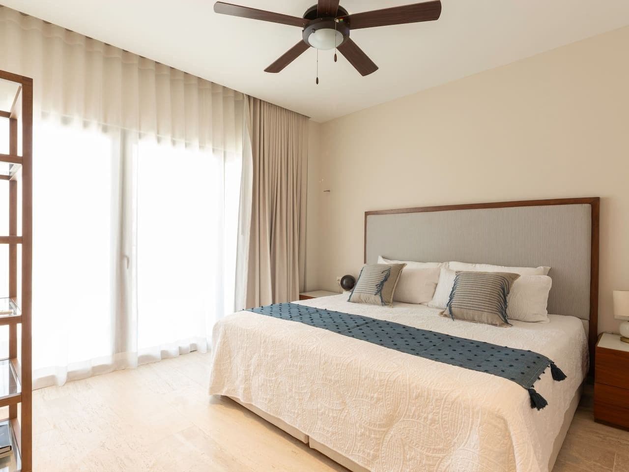 A hotel room with a bed, a ceiling fan, a nightstand, and a window with curtains.