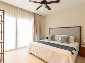 A hotel room with a bed, a ceiling fan, a nightstand, and a window with curtains. - Kanaa Marina - Luxury Oceanview Residence (Progreso)