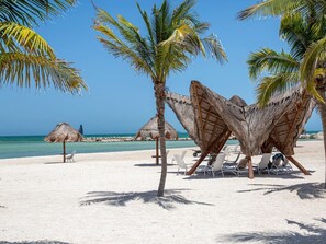 A beach with thatched umbrellas and lounge chairs, a clear blue sky, and a calm sea. - Kanaa Marina - Luxury Oceanview Residence (Progreso)