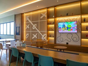 A modern interior with a long wooden table, teal chairs, a television displaying animated characters, and a wall with geometric patterns. - Kanaa Marina - Luxury Oceanview Residence (Progreso)