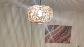 Quarto com sofá de couro preto, tapete marrom e laranja, planta em vaso, escrivaninha com luminária e um quadro na parede.