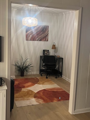 A room with a modern desk, a potted plant, a patterned rug, and a hanging light fixture.
