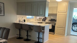 Cozinha com ilha central, banquetas de bar e área de jantar com tapete.