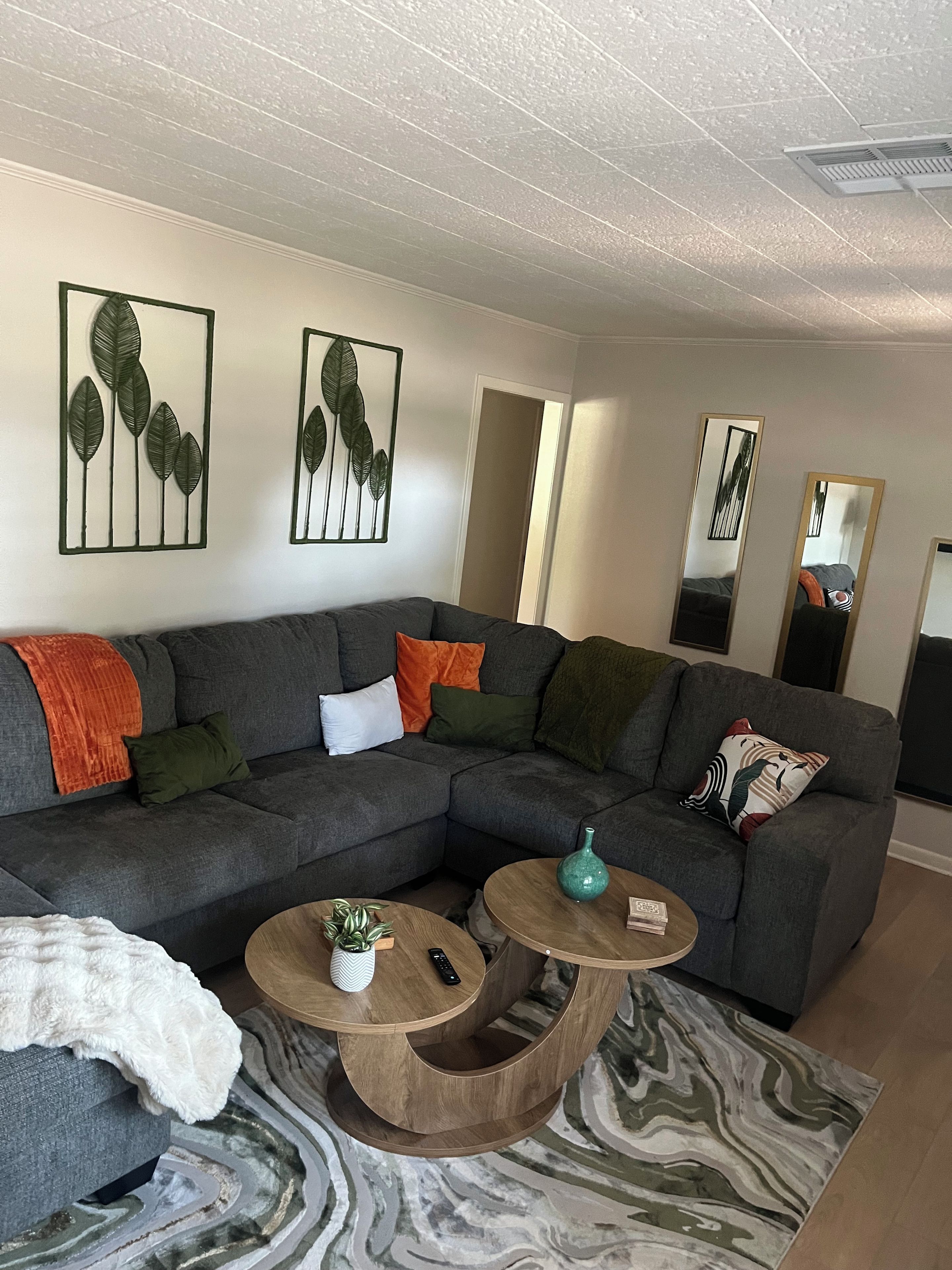 Una sala moderna con un sofá modular, dos mesitas auxiliares y un adorno de hojas en la pared.