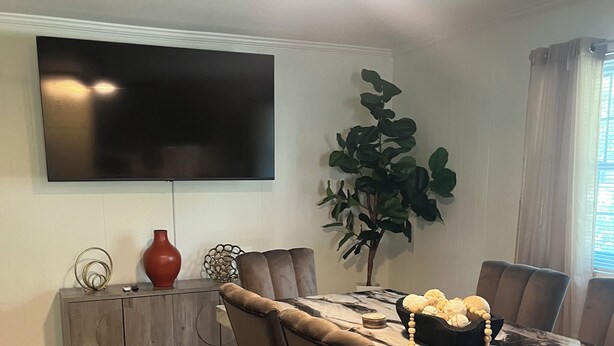 Uma área de refeições com mesa de mármore, cadeiras estofadas, televisão na parede e ventilador de teto.