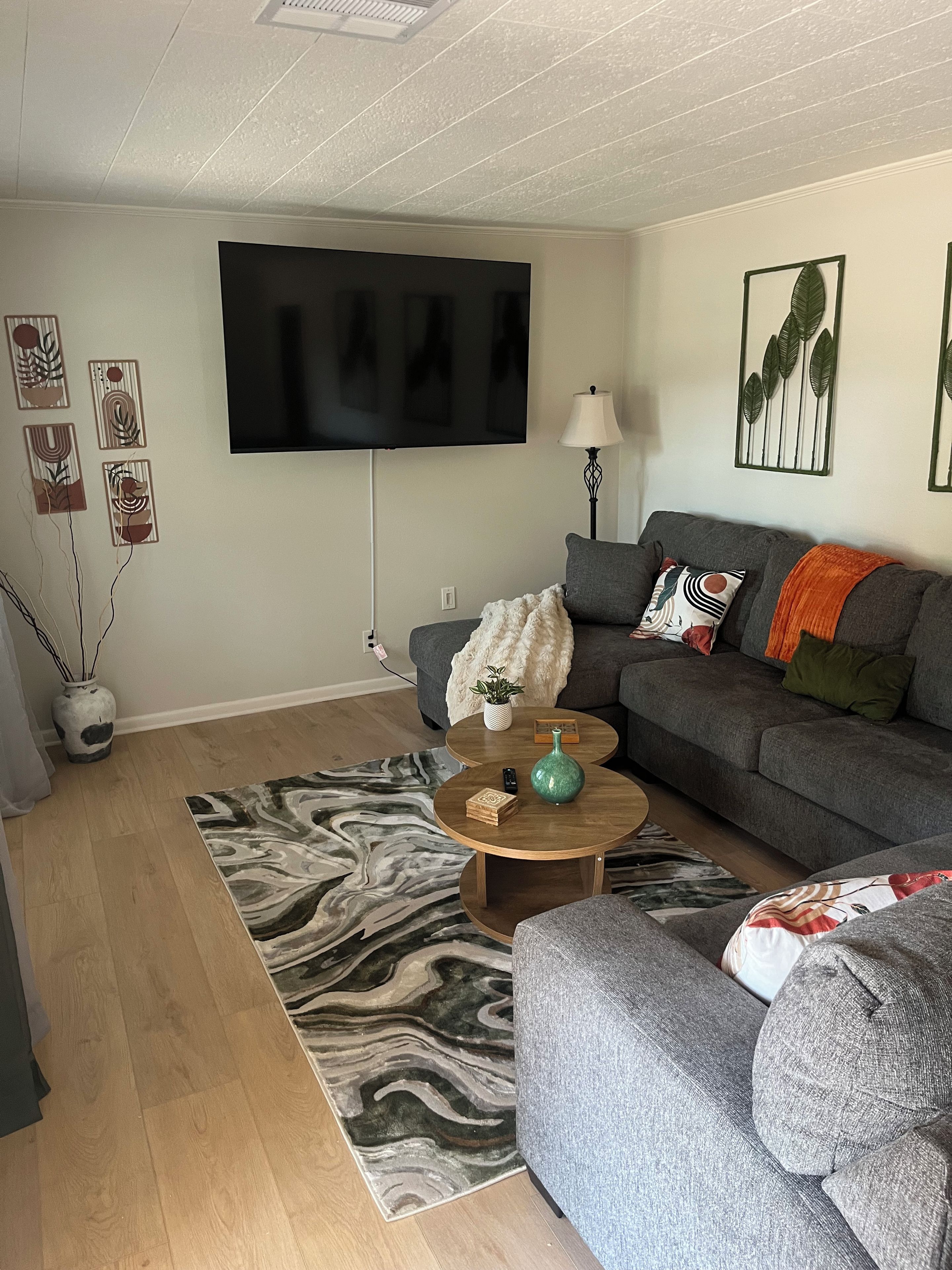 Un soggiorno con una TV a schermo piatto montata a parete, un divano grigio con cuscini, un tavolino da caffè con oggetti decorativi e un tappeto decorato.