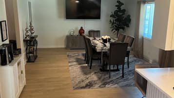 Un salón comedor amplio con televisión de pantalla plana montada en la pared y ventilador de techo.