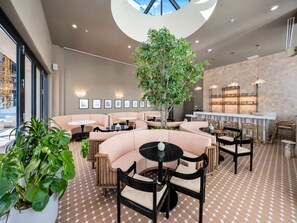 Ein stilvoller Lounge-Bereich mit geschwungenen Sitzgelegenheiten, einem zentralen Baum und einer Bar mit Pendelleuchten.