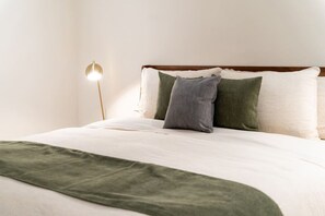Een keurig opgemaakt bed met een groene plaid, een bedlampje en twee kussens.