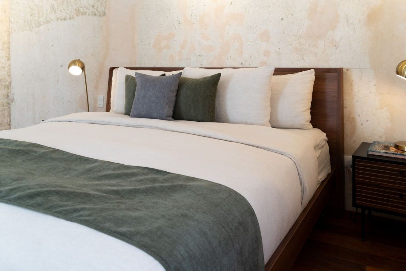 A neatly made bed with a green throw blanket, a wooden headboard, and two bedside lamps.
