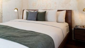 A neatly made bed with a green throw blanket, a wooden headboard, and two bedside lamps.