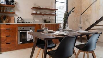 A modern kitchen with wooden cabinets, a dining table set for four, and a staircase in the background.