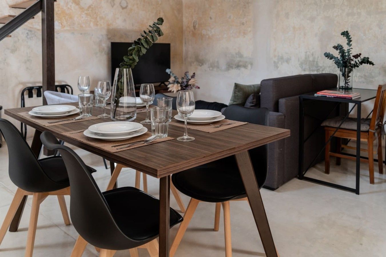 Un coin repas avec une table en bois dressée pour quatre personnes, des chaises noires et un canapé en arrière-plan.