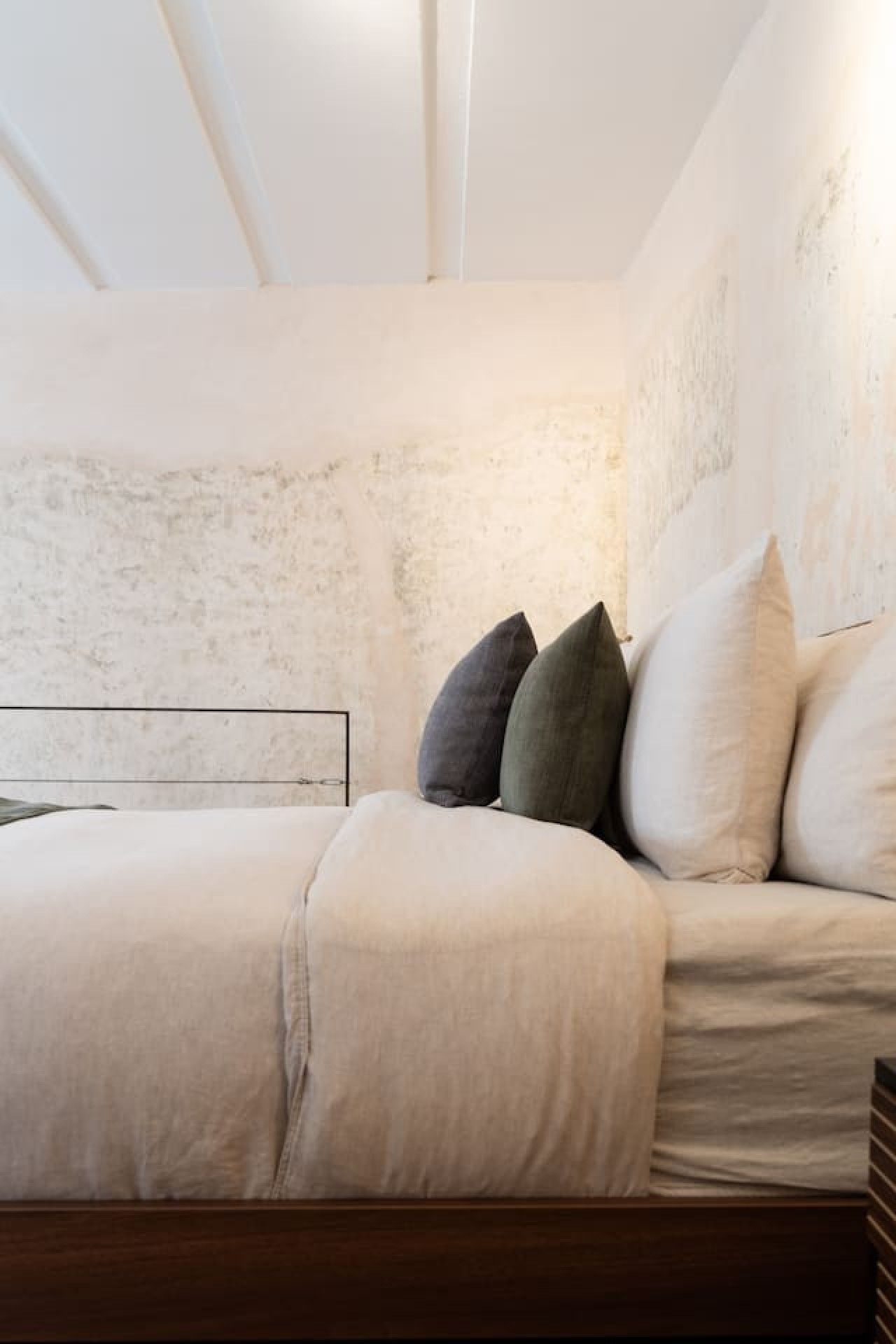 Une chambre à coucher moderne au design minimaliste, comprenant un lit avec une tête de lit en bois, un mur à texture et une table de chevet simple.