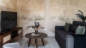 Un salon comprenant un téléviseur, un canapé, une table basse avec des livres et un vase, ainsi qu’un fauteuil.