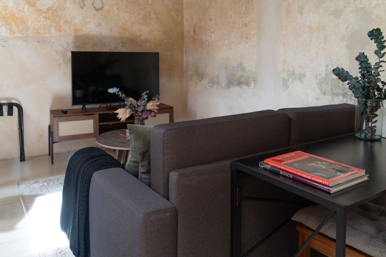Un salon moderne comprenant un canapé, une table basse, un téléviseur à écran plat et un vase avec des fleurs.