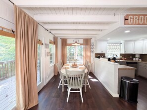 A dining area with a table and chairs, a kitchen with white cabinets, and a trash can. - Heavenly Honey Bear | Helen Getaway w/ Fire Pit (Helen)