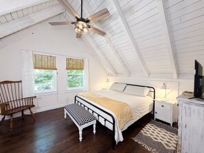 A bedroom with a sloped ceiling, a bed, a bench, a nightstand, a television, and a window with blinds. - Heavenly Honey Bear | Helen Getaway w/ Fire Pit (Helen)