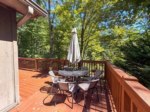 A wooden deck with a round table and chairs, surrounded by a wooden railing, overlooking a forested area. - Heavenly Honey Bear | Helen Getaway w/ Fire Pit (Helen)