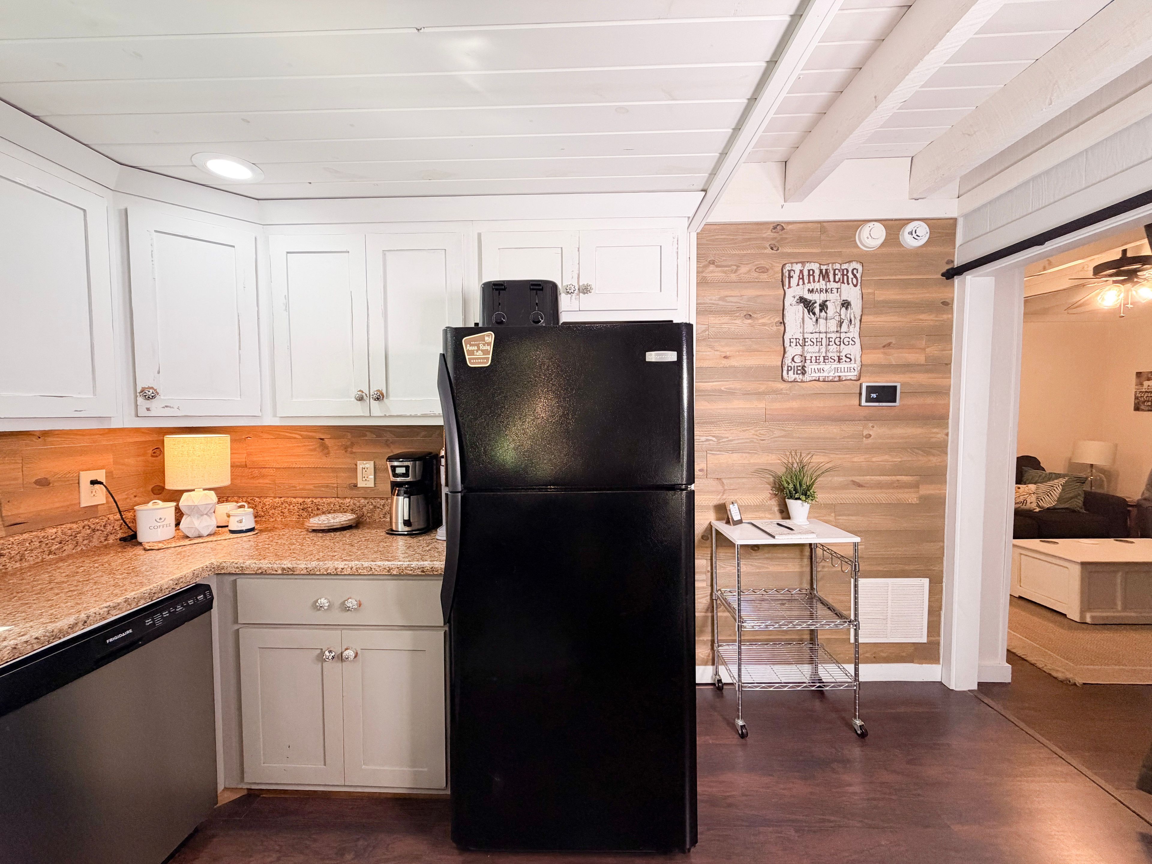 A kitchen with white cabinets, a black refrigerator, a coffee maker, and a small table with a plant.