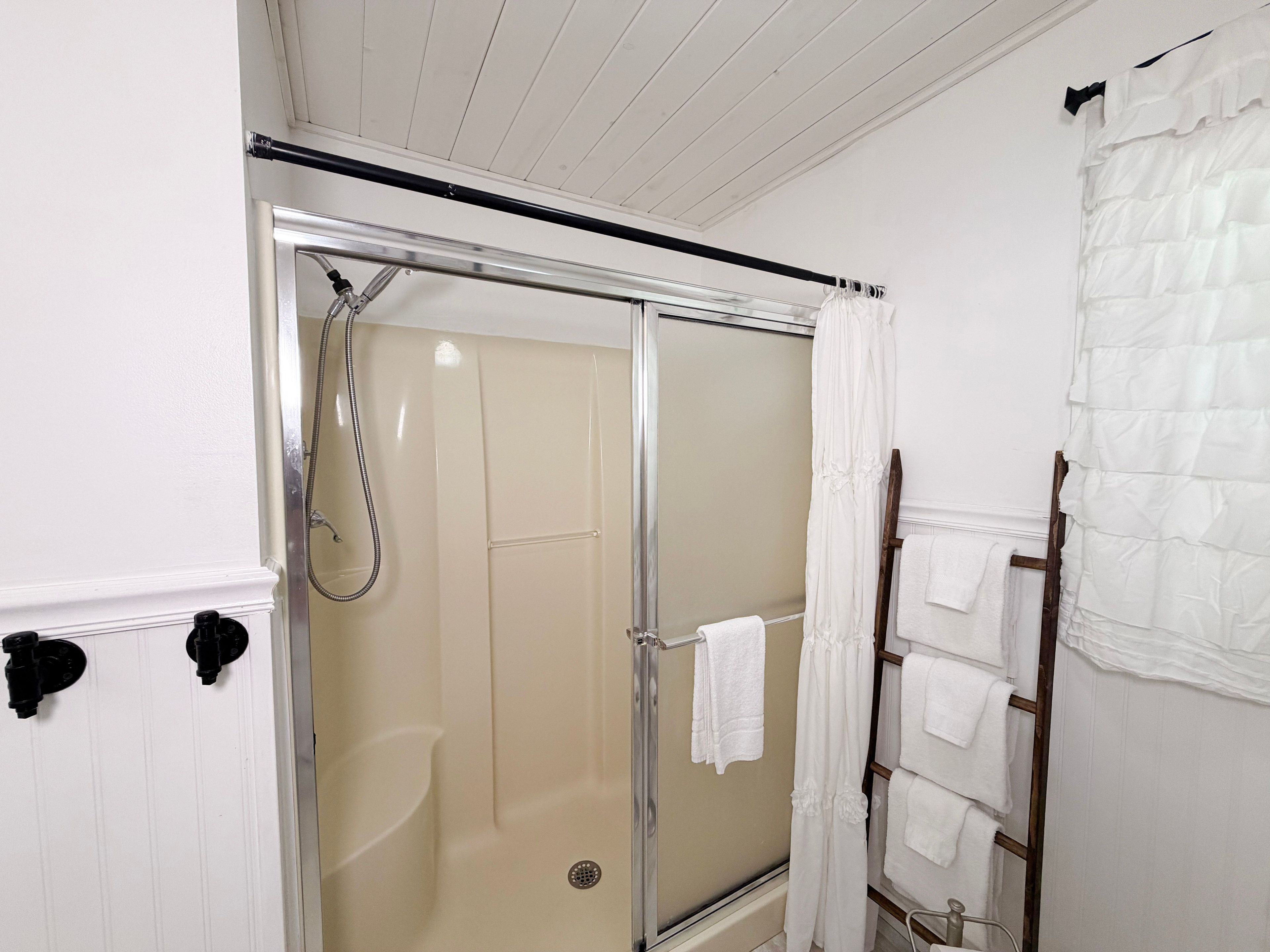 Ett badrum med en dusch som är avskärmad med glasväggar, en handduksställning och en trästege.