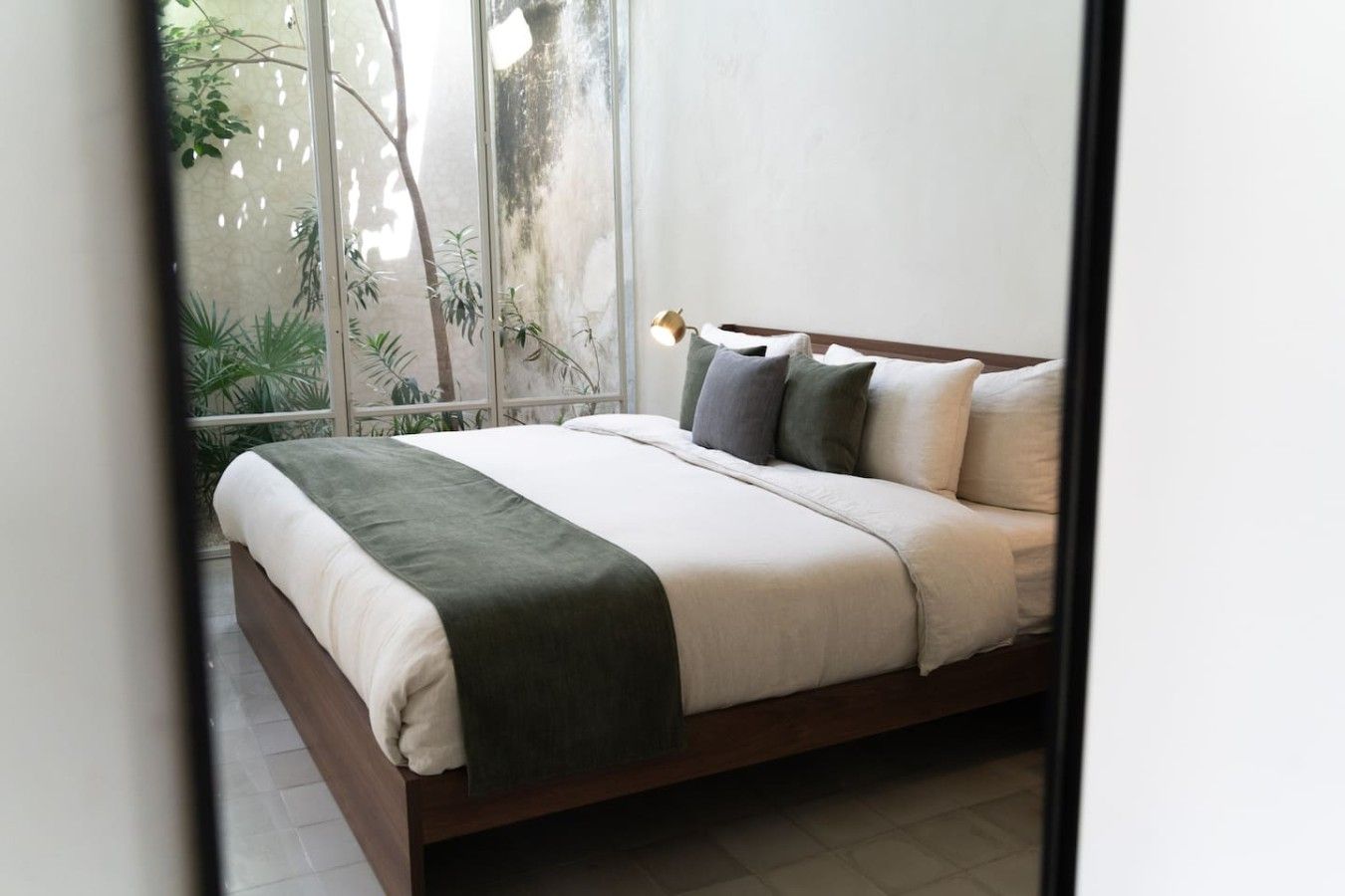 Ein Schlafzimmer mit einem Bett, Kissen und Blick auf Grün durch ein Fenster.