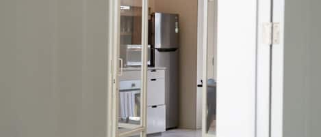 Un pasillo que conduce a una cocina equipada con nevera, microondas y armarios.