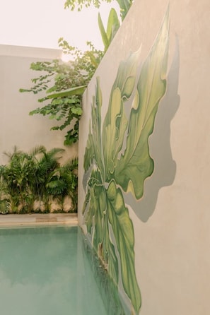 Piscina com um mural de folhas grandes na parede adjacente.