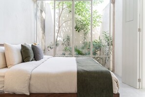 Ein Schlafzimmer mit einem Bett, Kissen, einem Fenster und Blick auf Grünfläche.