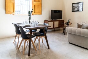 Ein Essbereich mit Tisch für vier Personen, einem Fernseher auf einem Schrank und einer Couch im Wohnbereich.