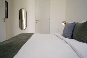 Een slaapkamer met een bed, een bedlampje, een spiegel en een deur.