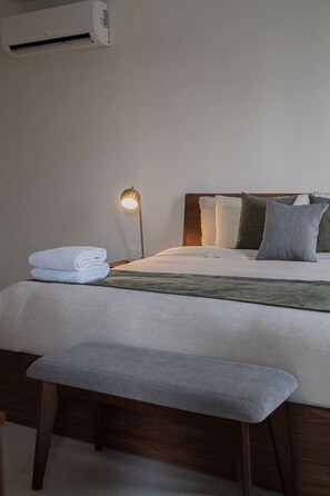 A neatly made bed with pillows and a folded towel, a bedside lamp, and a wooden bench. - Izamal · 2 rec · 2 baños · Tina en rooftop (Mérida)