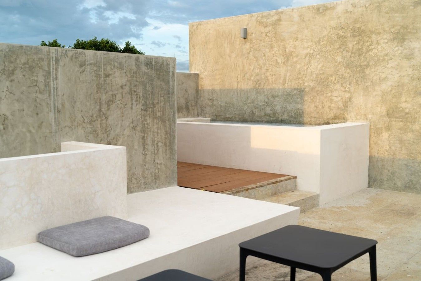 A modern outdoor seating area with concrete walls, a wooden deck, and a black table.