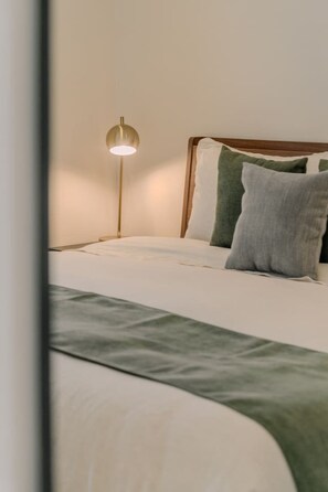 A neatly made bed with a white and green bedspread, a wooden headboard, and a floor lamp with a round shade. - Izamal · 2 rec · 2 baños · Tina en rooftop (Mérida)