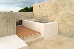 A modern outdoor space with a concrete wall, a wooden deck, and a rectangular pool area. - Izamal · 2 rec · 2 baños · Tina en rooftop (Mérida)