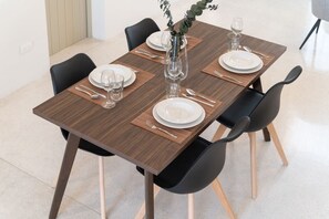 A rectangular dining table with four chairs, each with a black seat and wooden legs. The table is set with white plates, cutlery, and clear glasses. - Izamal · 2 rec · 2 baños · Tina en rooftop (Mérida)