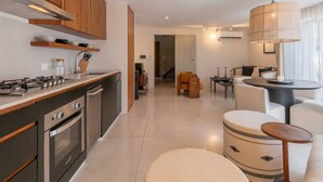 Cozinha moderna com eletrodomésticos embutidos, sala de jantar com mesa redonda e área de estar com sofá e pufe.