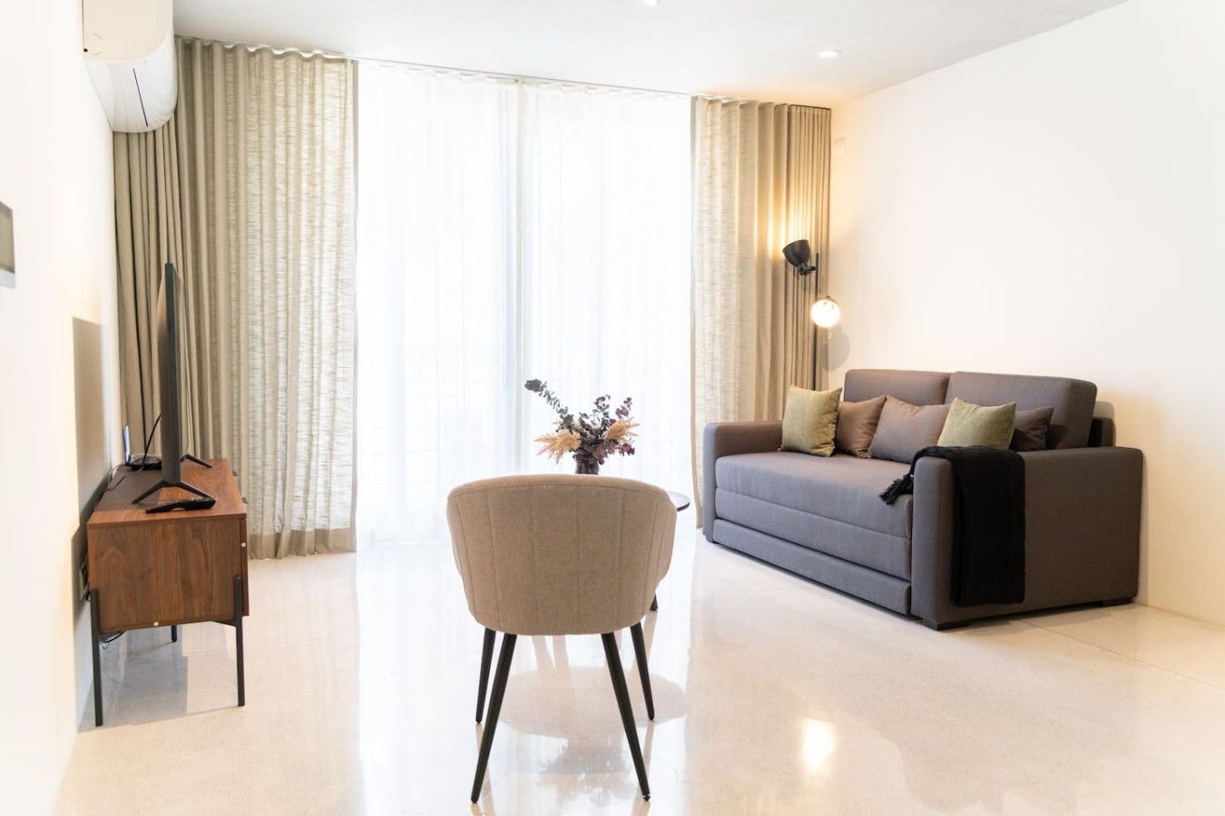 Uma sala de estar moderna com um sofá, uma poltrona, um rack para TV e uma luminária.