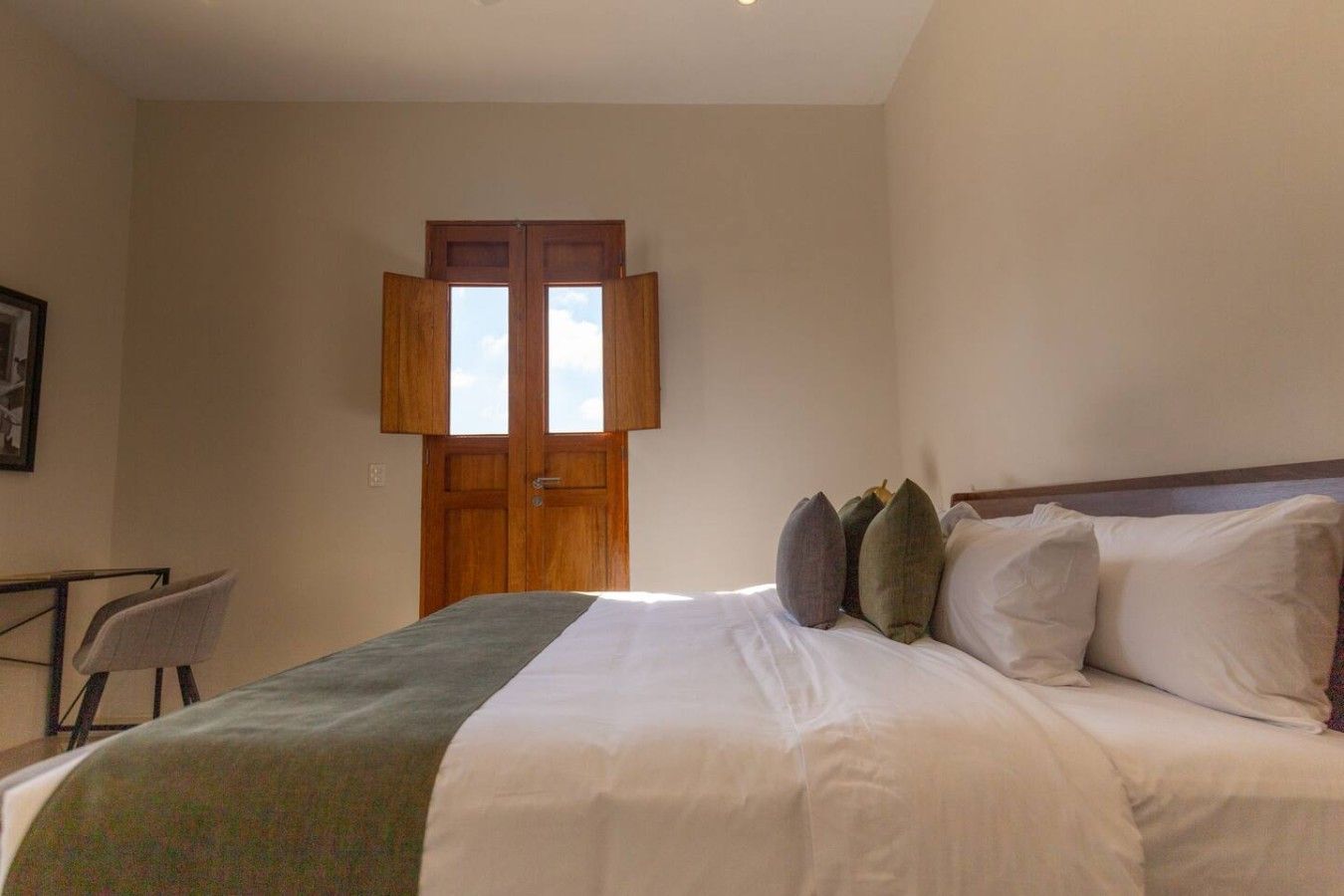 Een slaapkamer met een bed, kussens, een bureau en een raam met openslaande luiken.