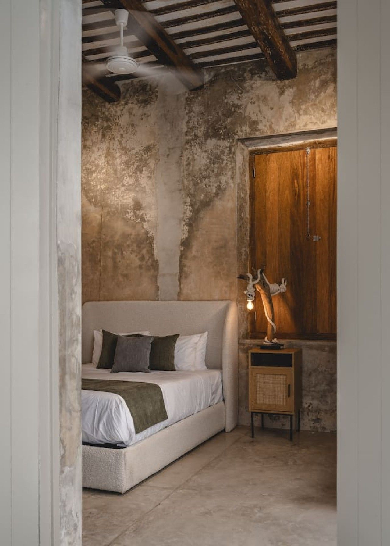 A bedroom with a bed, a nightstand, a lamp, and a wooden wardrobe.