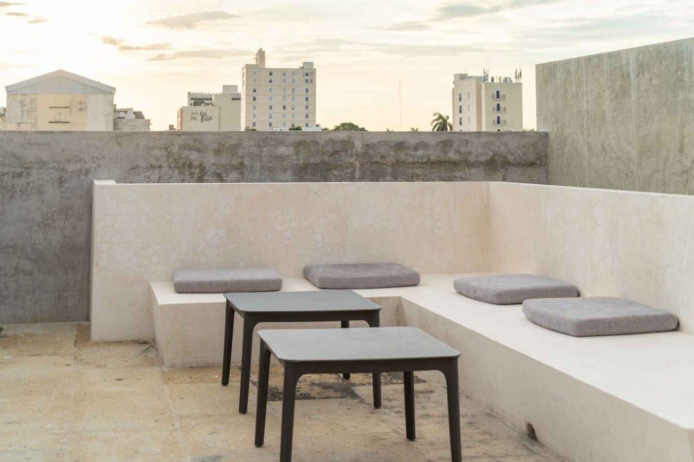 A rooftop terrace with a seating area consisting of a bench and two square tables.