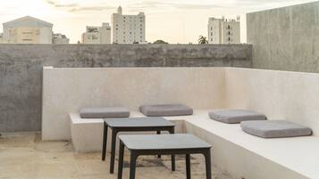 A rooftop terrace with a seating area consisting of a bench and two square tables.