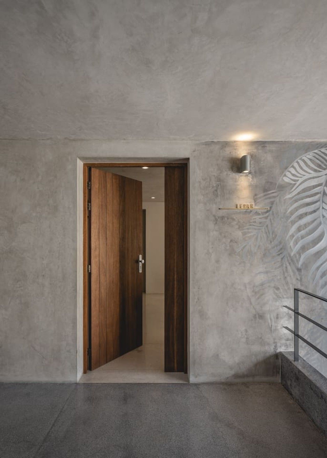 A hallway with a wooden door leading to another room, a textured wall, and a metal railing.