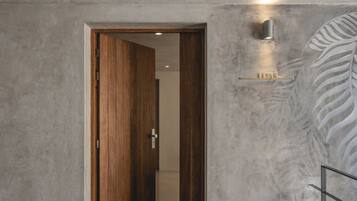 A hallway with a wooden door leading to another room, a textured wall, and a metal railing.
