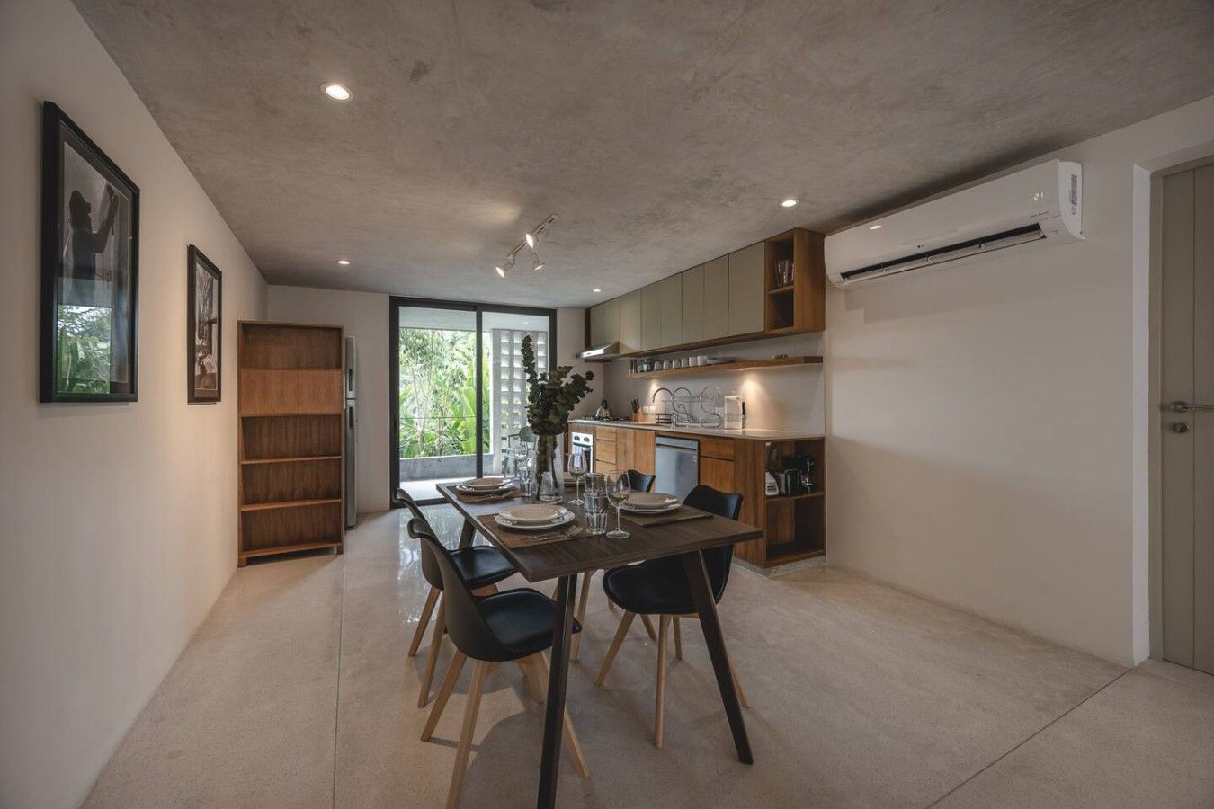 A modern kitchen with a dining area, featuring a built-in oven, a sink, and a window with a view of greenery.