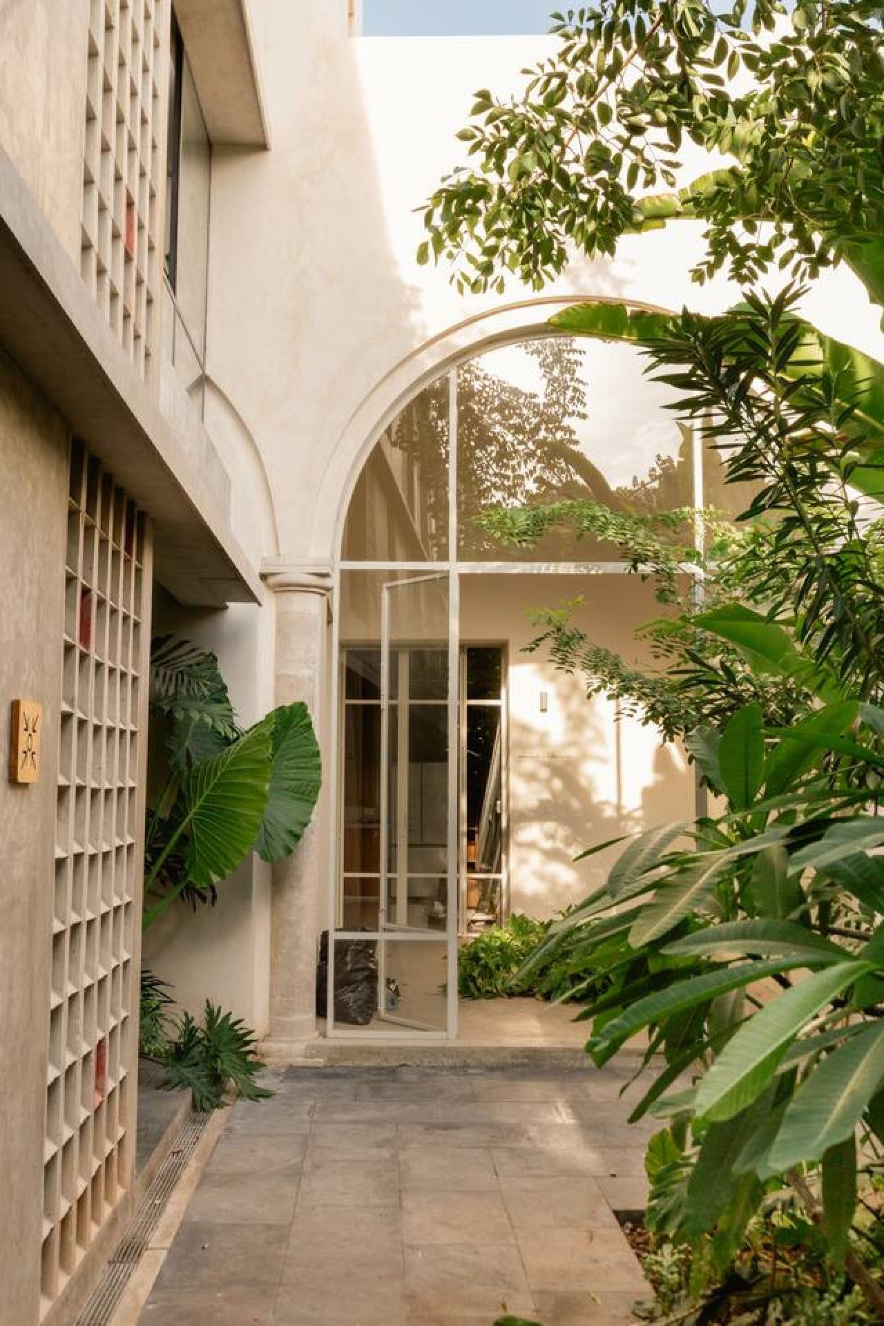 A building with a curved glass entrance, a tiled patio, and lush greenery.