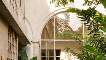 A building with a curved glass entrance, a tiled patio, and lush greenery.