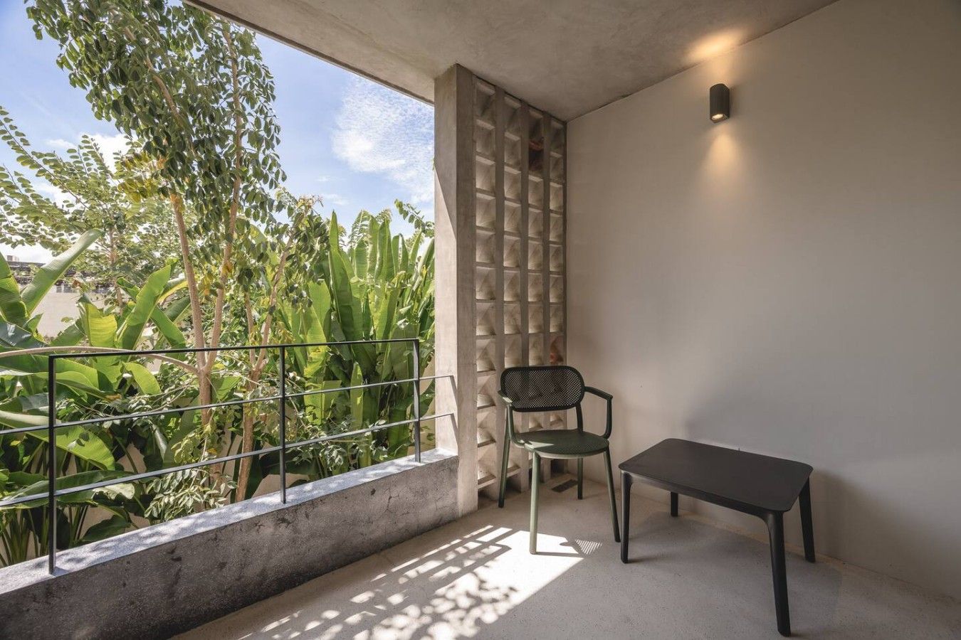 A balcony with a chair and table, a concrete floor, and a view of greenery.