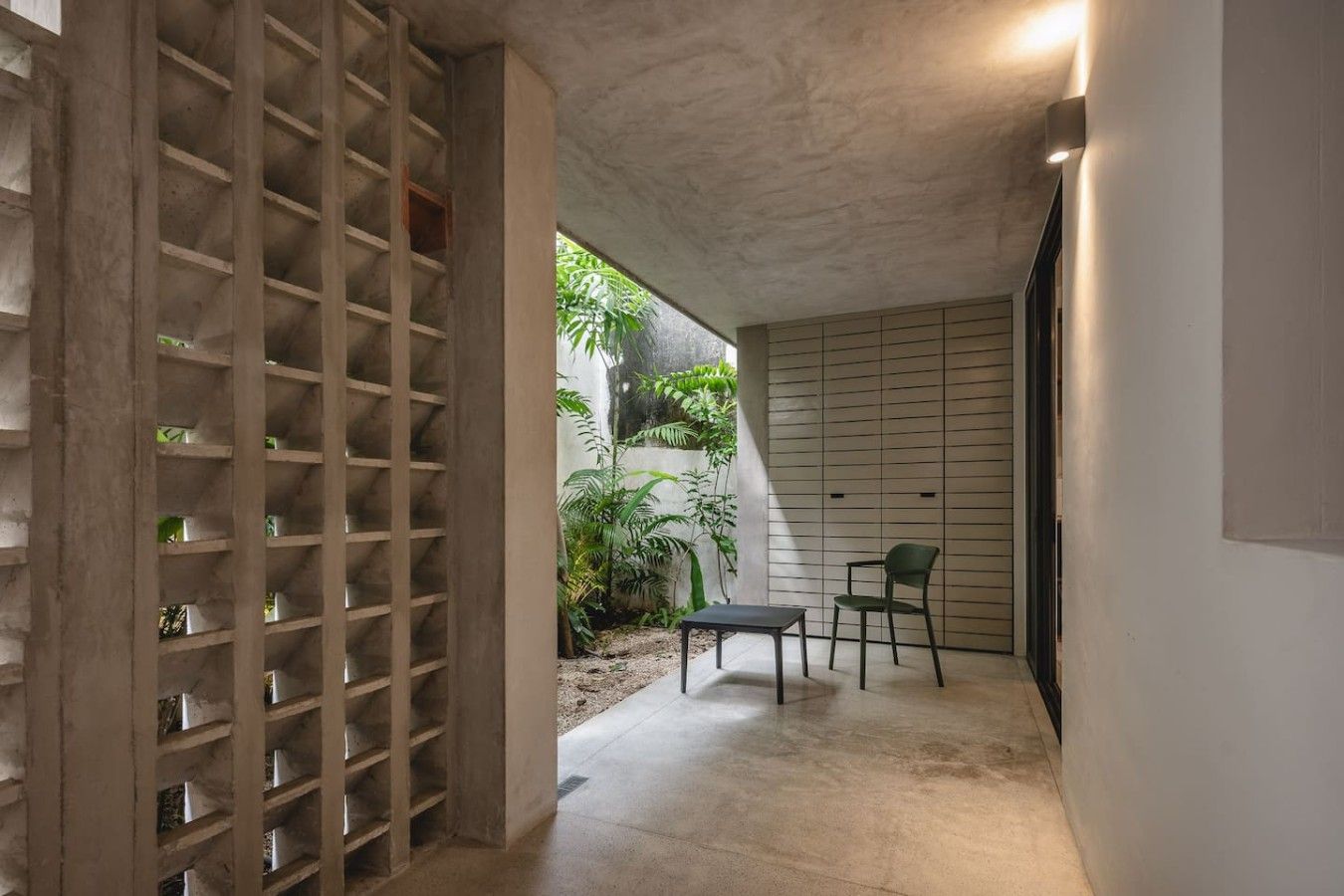 A corridor with a concrete floor, a wooden shelving unit, a green chair, and a table.